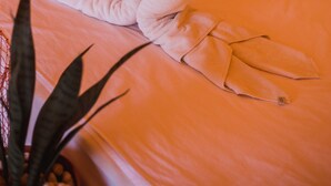A bed with a towel arranged in a heart shape, a chair, a small table, and a potted plant. - Roost Glamping (Rawai)