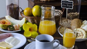 Una mesa de desayuno con una taza de café, jugo de naranja, pan y varias frutas.