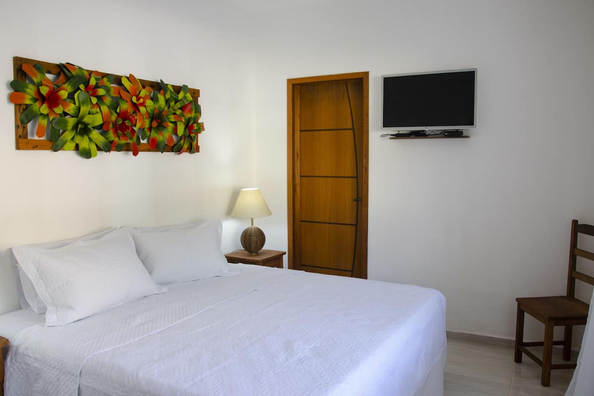 A bedroom with a bed, a wall-mounted TV, a wooden door, and a wall art piece.