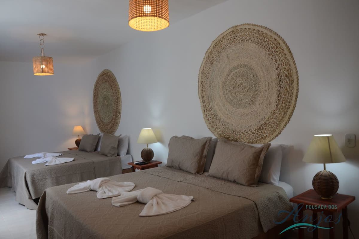 A hotel room with two beds, each with a large woven headboard, a bedside table with a lamp, and a hanging light fixture.