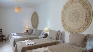 Habitación de hotel con tres camas, cada una con cubrecama y almohadas color beige. Hay dos mesitas de noche con lámparas, y un tapiz grande tejido sobre las camas.
