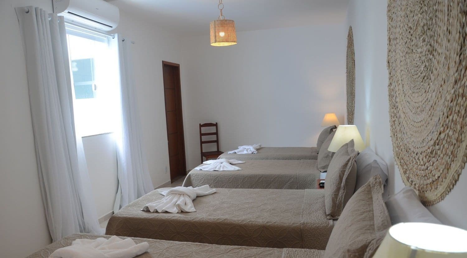 A hotel room with two beds, a standing lamp, a woven wall hanging, and a window with curtains.