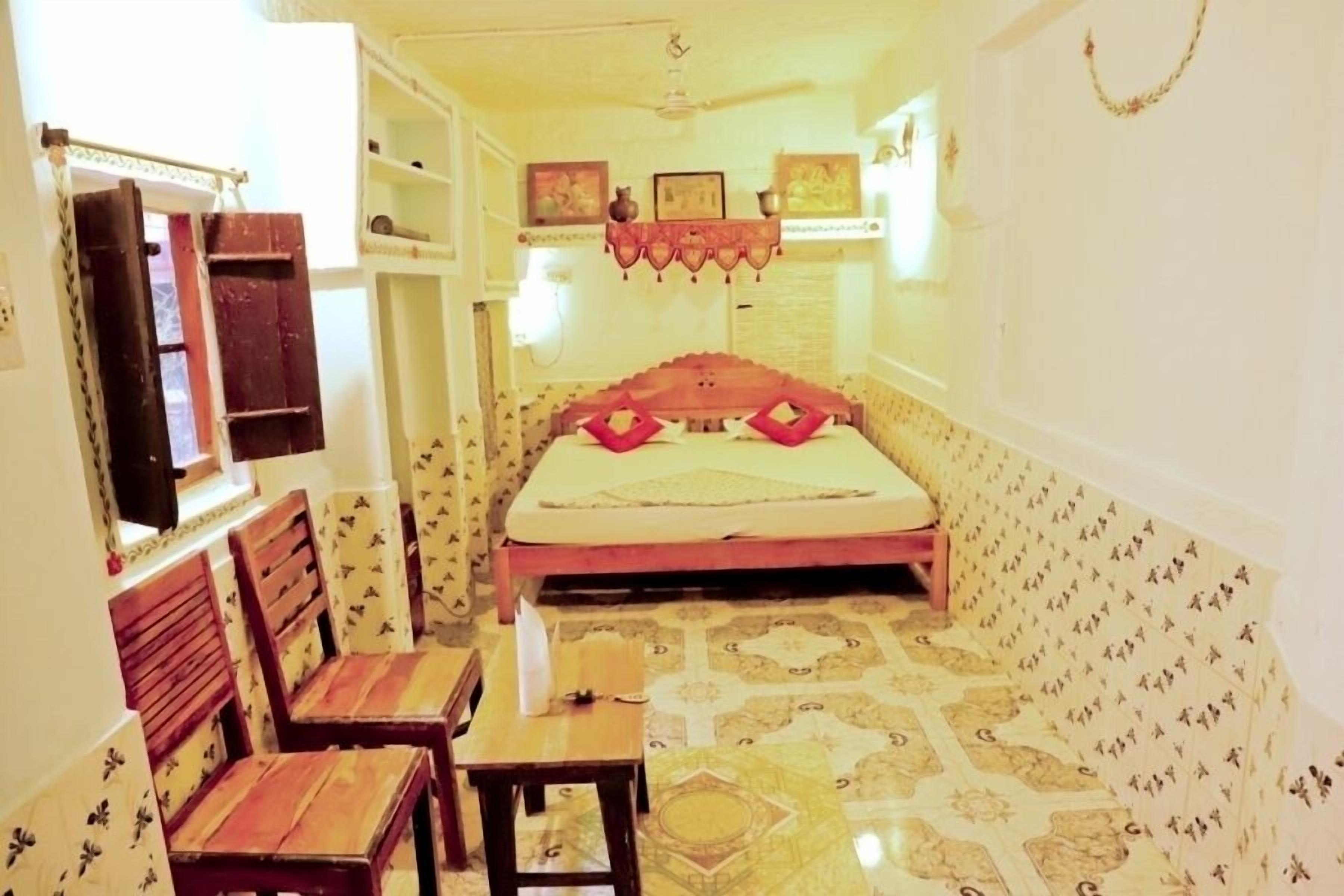 A room with a bed, a chair, a small table, and a shelf with decorative items.