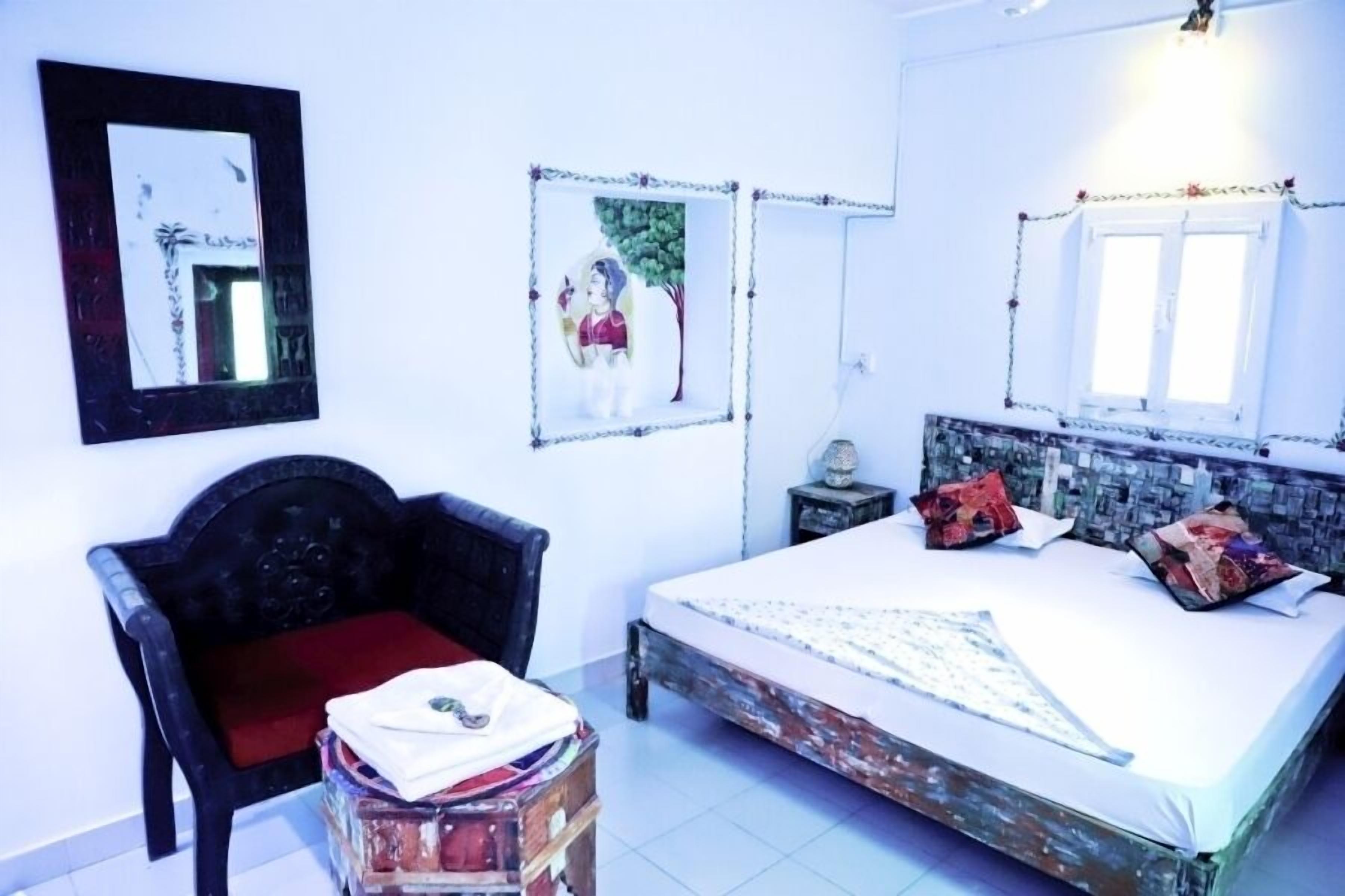 A bedroom with a bed, a chair, a small table, and two framed pictures on the wall.