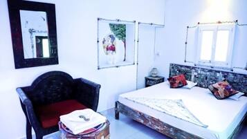 Un dormitorio con una cama, una silla, una mesita y dos cuadros en la pared.