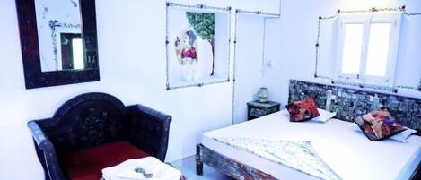 A bedroom with a bed, a chair, a small table, and two framed pictures on the wall.