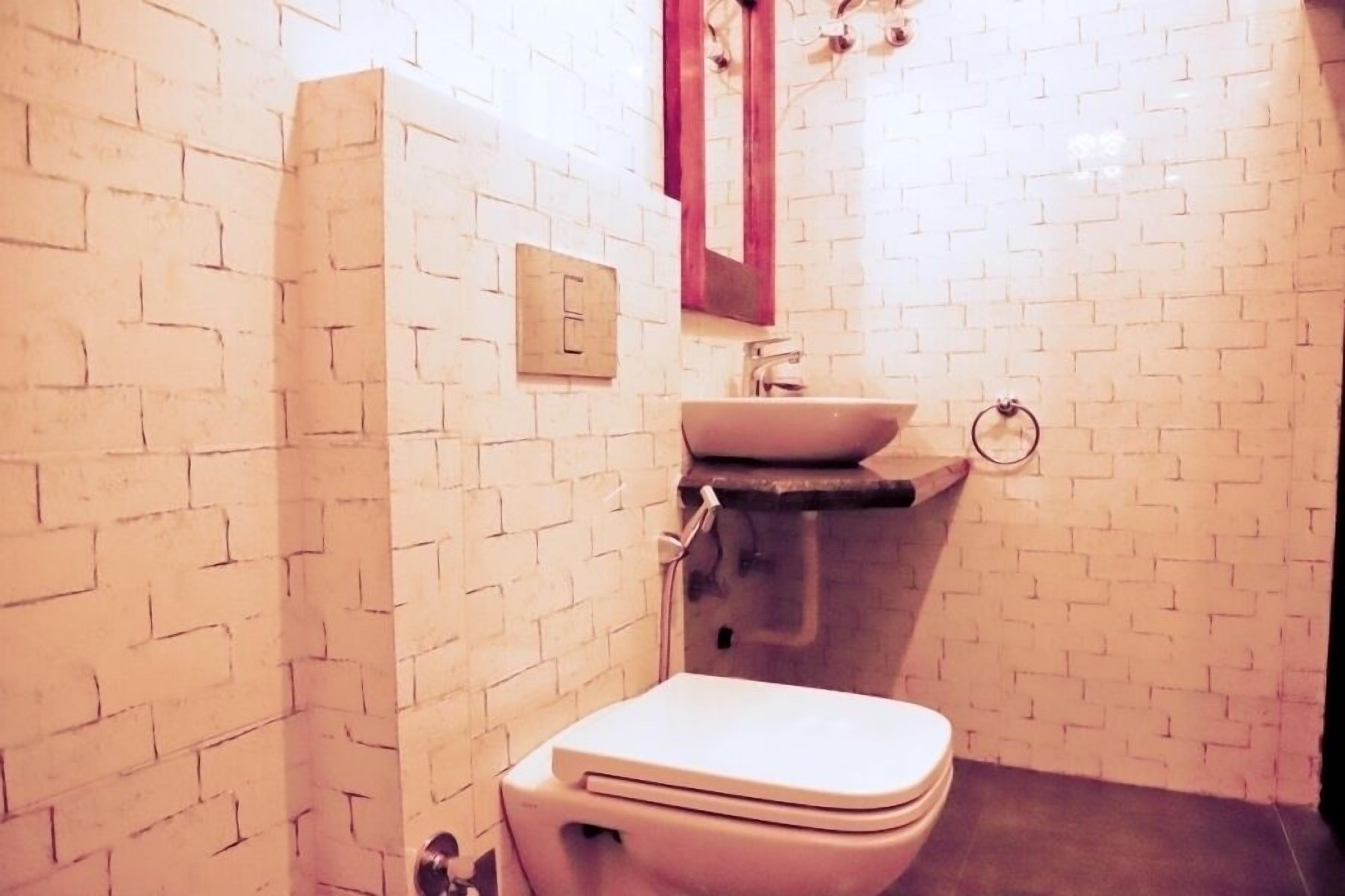 Un baño con paredes de ladrillo blanco, un inodoro blanco, un lavamanos y un espejo.