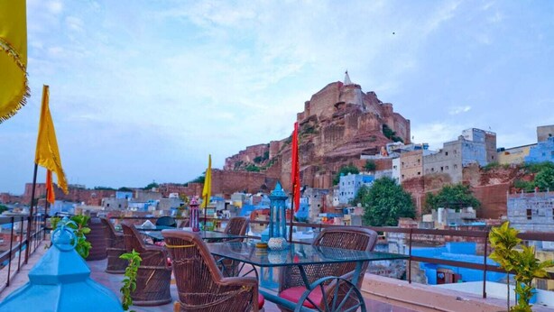 A rooftop terrace with wicker furniture, a glass table, and potted plants. - Singhvi's Haveli (Jodhpur)