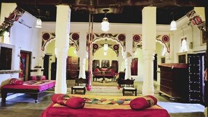 A traditional room with a bed, chairs, and a mirror. - Singhvi's Haveli (Jodhpur)