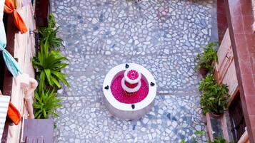 Un patio con una fuente central rodeada de mosaicos, plantas en macetas y un edificio con puerta de madera.