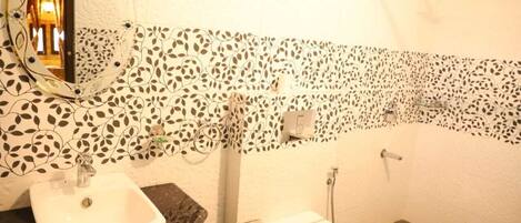 A bathroom with a white sink, toilet, and shower. The walls have a leaf-patterned tile design.
