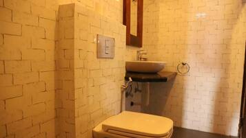 Un baño con pared de ladrillo blanco, inodoro blanco, lavamanos y espejo.