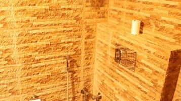 Une salle de bain avec un mur en pierre, des toilettes, une douche et un distributeur de serviettes.