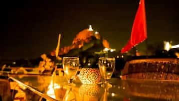 A table with two glasses and a decorative item, set against a night scene with a dome-shaped structure and a red flag in the background.