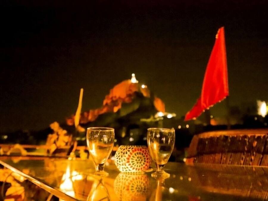 A table with two glasses and a decorative item, set against a night scene with a dome-shaped structure and a red flag in the background.