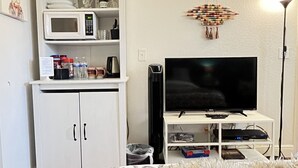 A living room with a white cabinet, microwave, flat-screen TV, and a small shelf with decorative items. - New Studio  - Minutes to Convention Center, Disney,Universal ,INTL DR (Orlando)