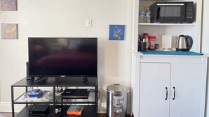 A living room with a flat-screen TV, a coffee maker, a microwave, and a cabinet with kitchen items. - New Studio  - Minutes to Convention Center, Disney,Universal ,INTL DR (Orlando)