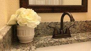 A bathroom sink with a marble countertop, a dark faucet, and a vase with white flowers. - New Studio  - Minutes to Convention Center, Disney,Universal ,INTL DR (Orlando)