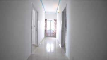 A hallway with white walls and a tiled floor, leading to a room with a window and curtains.