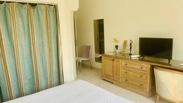 Habitación de hotel con cama, cómoda de madera con televisor, una silla y baño visible a través de una puerta abierta.