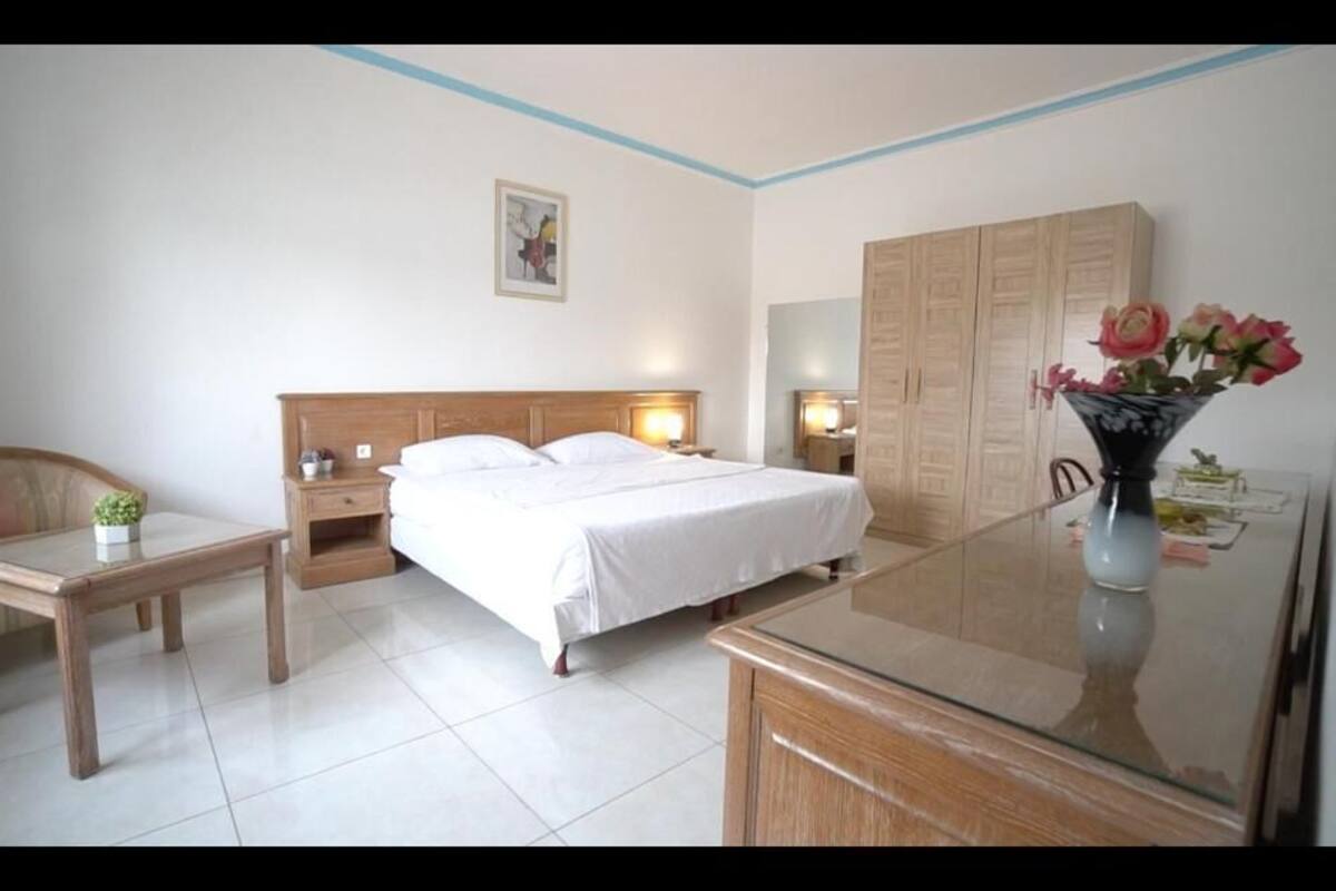 A hotel room with a bed, bedside tables, a desk, a chair, a wardrobe, and a vase with flowers.