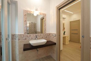 A modern bathroom with a large mirror, a white sink, and a wooden door in the background. - Relais Ohana (Vico Equense)