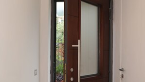 A hallway with a wooden door, a tiled floor, and a view of a garden through an open door. - Relais Ohana (Vico Equense)