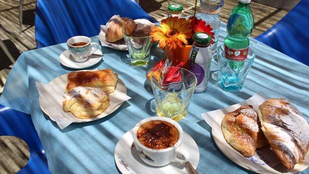 A table set with pastries, a cup of coffee, a glass of water, a bottle of water, and a flower arrangement. - Relais Ohana (Vico Equense)