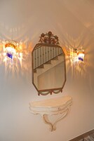 Un espejo adosado a la pared con un marco ornamentado, una escalera y dos apliques con lámparas decorativas.