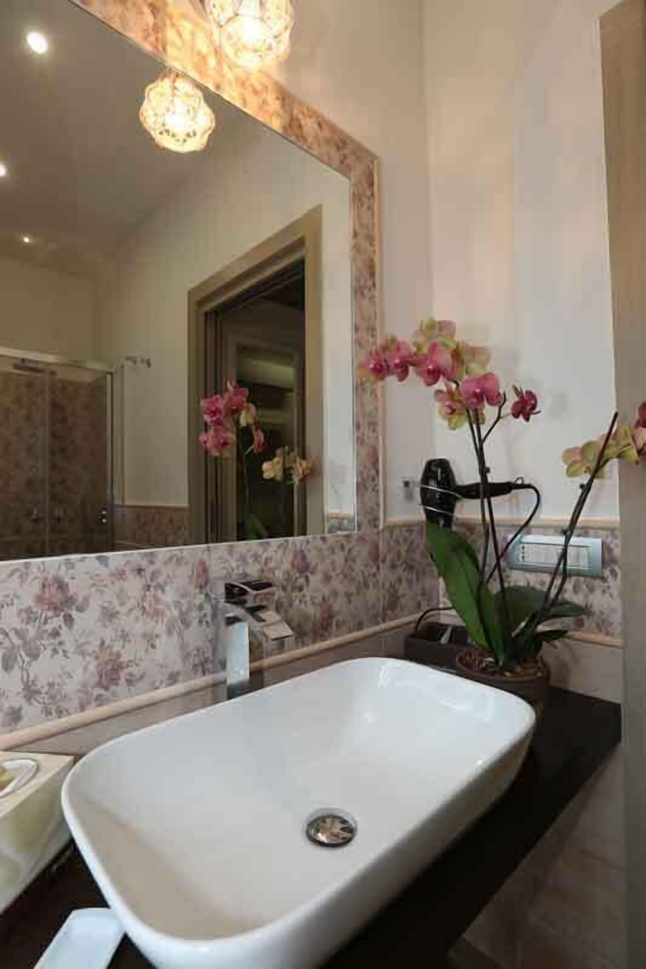 Ein Badezimmer mit einem großen, ovalen Waschbecken, einem Spiegel und zwei Orchideen.