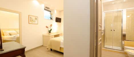 A modern hotel room with a bed, bedside table, and a shower area with a glass door.