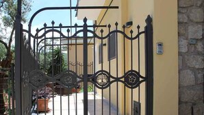 A wrought iron gate with decorative elements, leading to a building with a stone wall and a potted plant in the foreground. - Relais Ohana (Vico Equense)