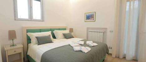 A neatly arranged bedroom with a bed, bedside tables, a radiator, and a window.