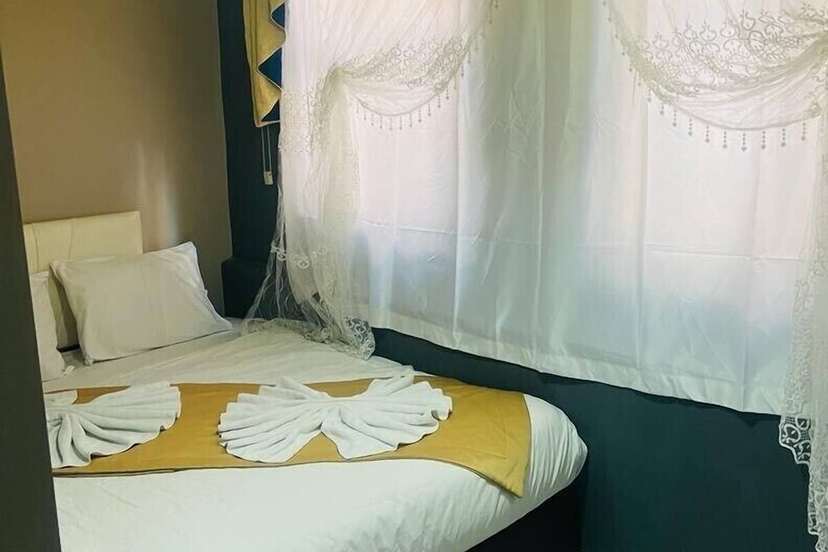A bedroom with a bed, white curtains, and a hanging light fixture.