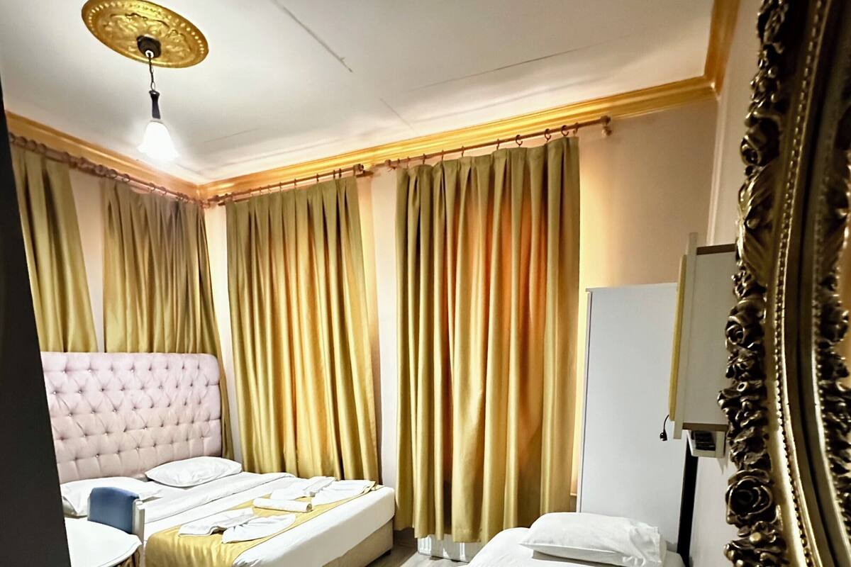 A hotel room with two beds, a desk, a chair, a mirror, and a ceiling fan.