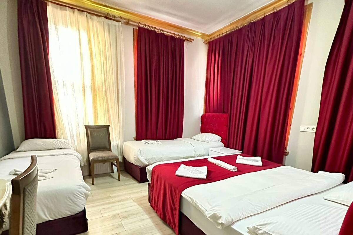 A hotel room with three beds, a wooden chair, and a desk.