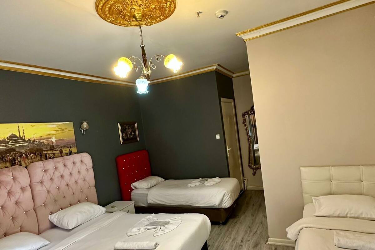 A hotel room with a large bed, a smaller bed, a red cabinet, and a chandelier.