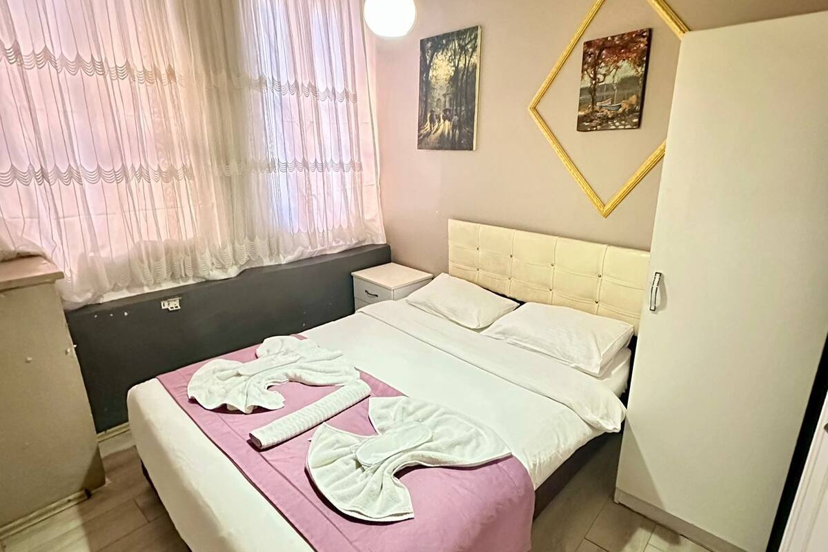 A bedroom with a bed, a window with curtains, a bedside table, and a wall-mounted picture frame.