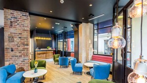 A modern lounge area with blue and green seating, a brick accent wall, and large windows. - Hotel Bridget (Paris)