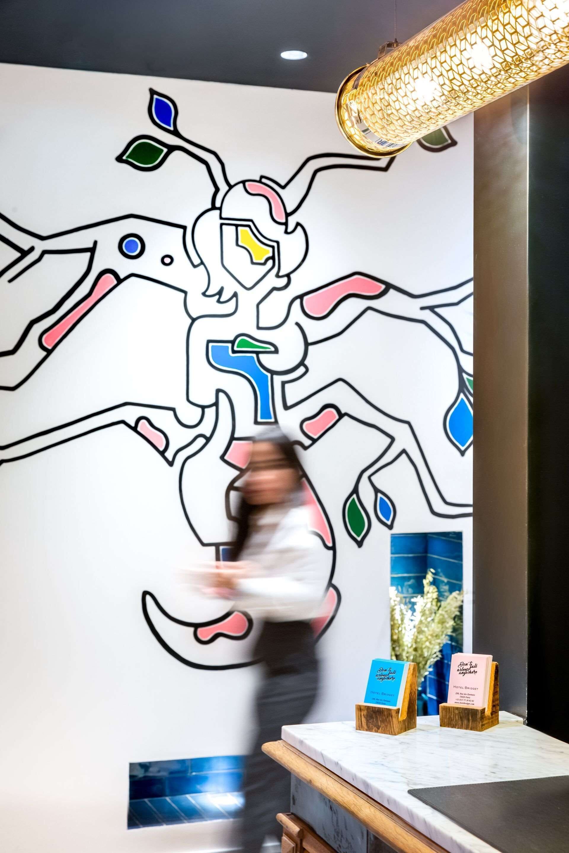 A wall with a colorful abstract design, a hanging light fixture, and two wooden nameplates on a marble counter.