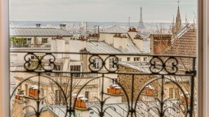 A view from a window with ornate metal bars, overlooking a cityscape with buildings and a distant tower. - Hotel Bridget (Paris)