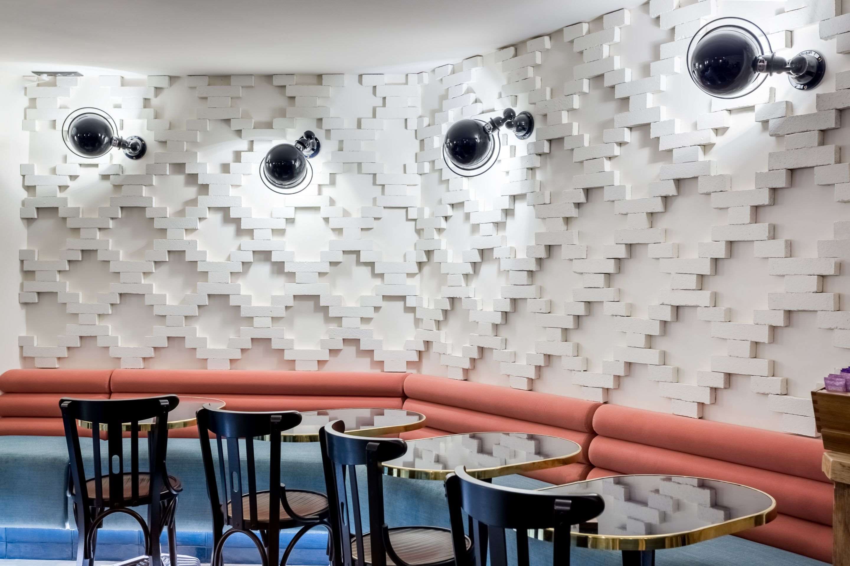 Et moderne interiør med et geometrisk vægdesign, et buet siddeområde og runde borde.