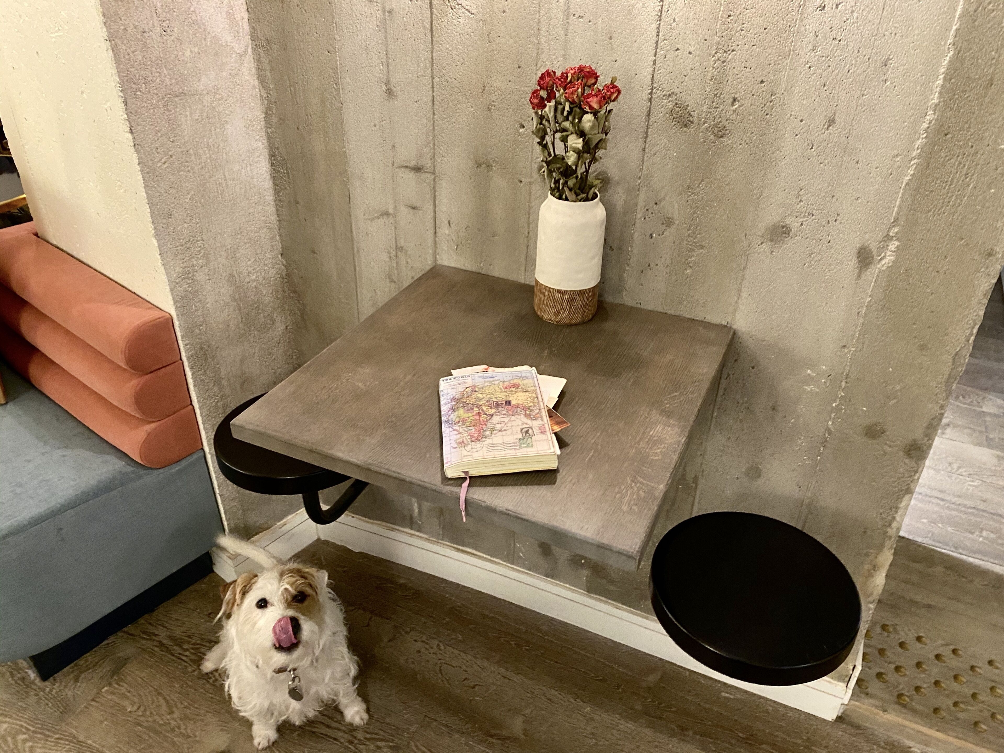 Une petite table carrée, sur laquelle se trouvent un vase de fleurs rouges, une carte et un tabouret noir.