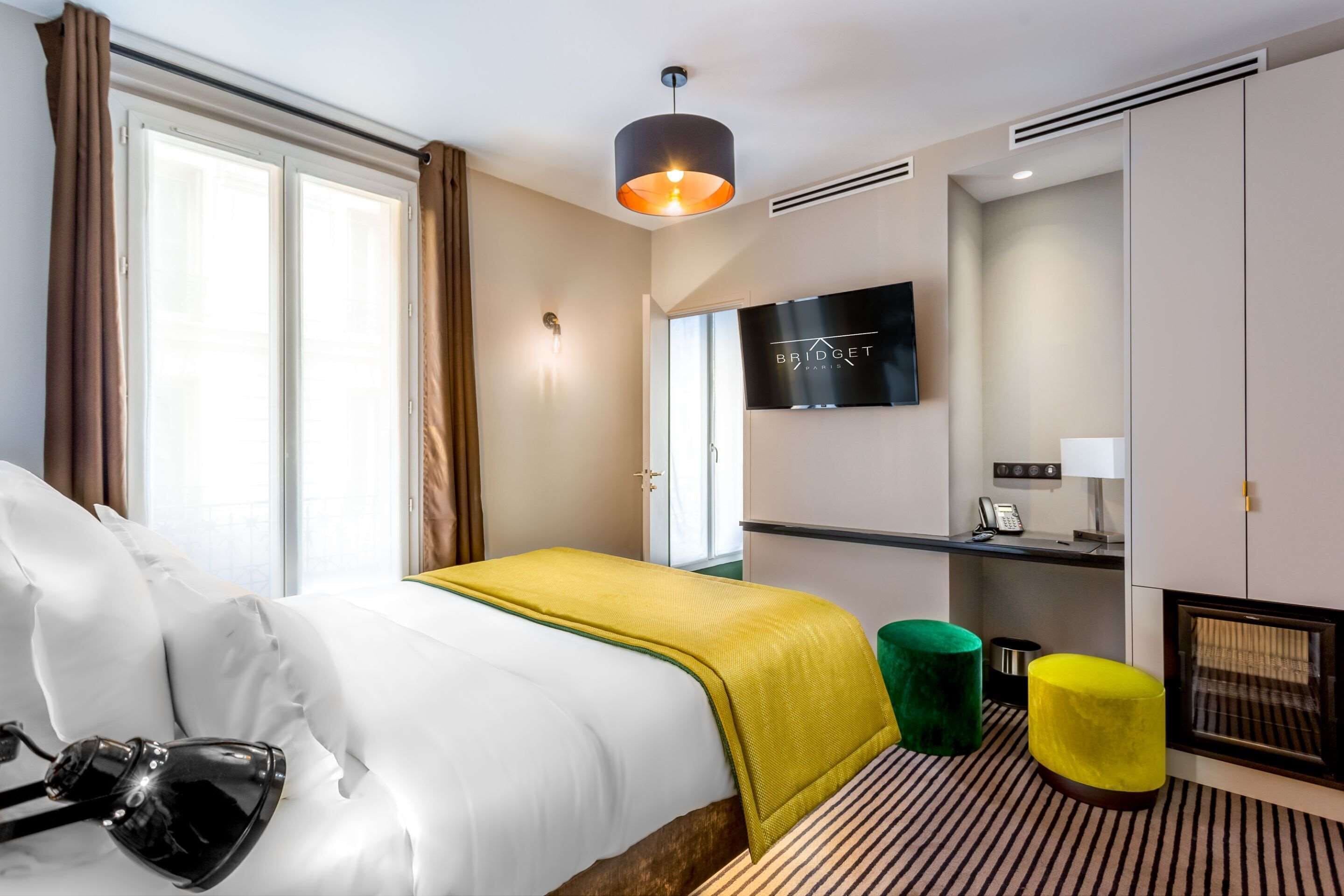 A hotel room with a bed, a desk, a television, and a window with curtains.