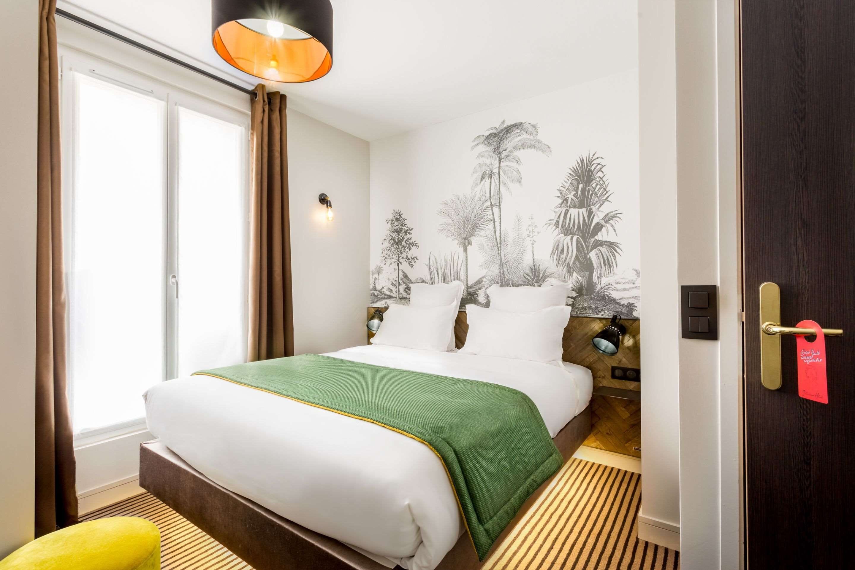 A hotel room with a bed, a nightstand, a lamp, a door with a tag, and a window with curtains.