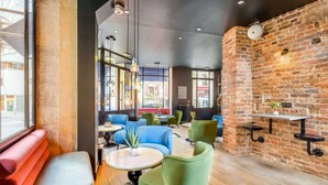 A modern interior with a brick wall, green and blue seating, and a large window offering a view of the street. - Hotel Bridget (Paris)