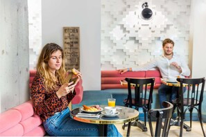 A modern cafe with a pink sofa, a round table, and a wall-mounted sign. - Hotel Bridget (Paris)