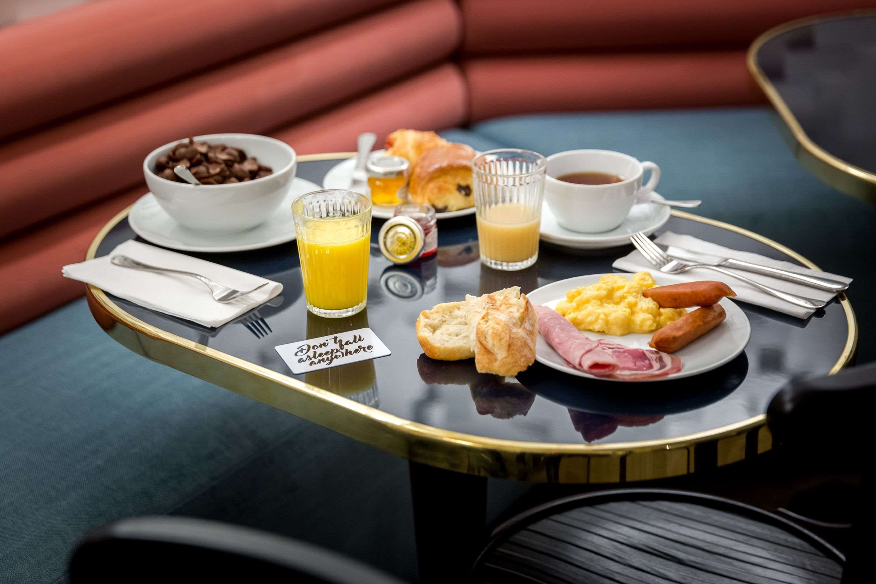 Een ontbijfwagen met koffie, sinaasappelsap, croissants en roerei op een tafel.