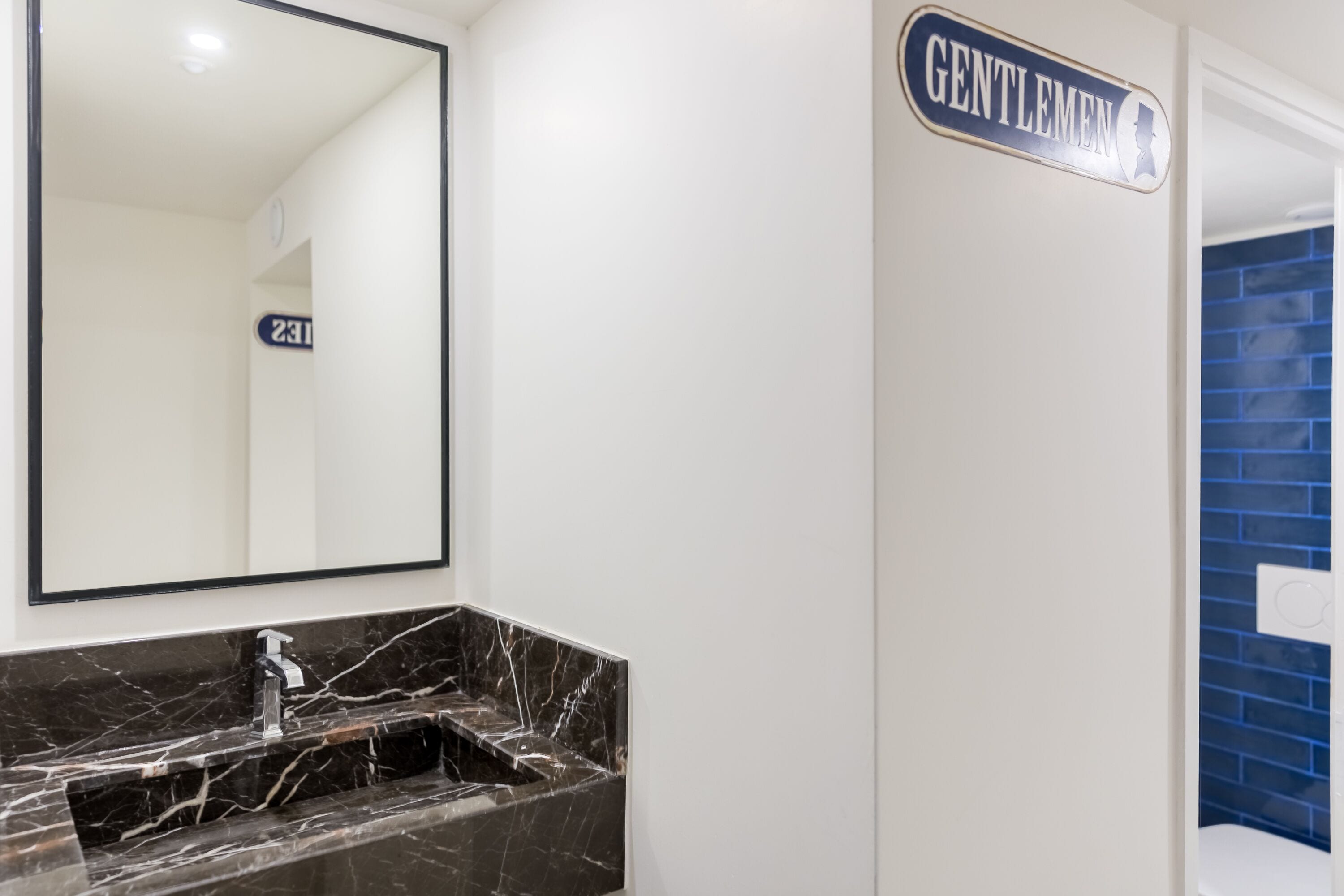 A bathroom with a marble sink, a mirror, and a sign that reads "GENTLEMEN'S".