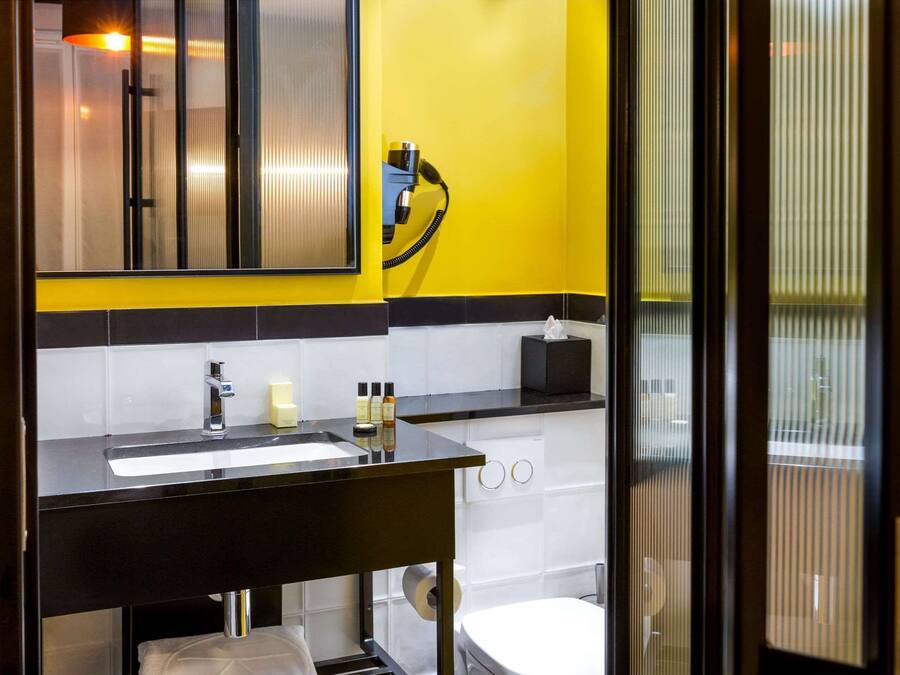 A modern bathroom with a black sink, white tiles, and a yellow accent wall.